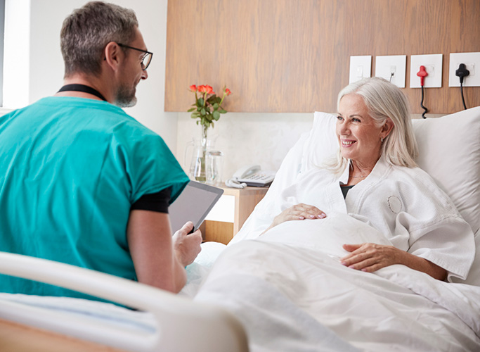 Surgeon With Digital Tablet Visiting And Talking With Mature Female Patient In Hospital Bed