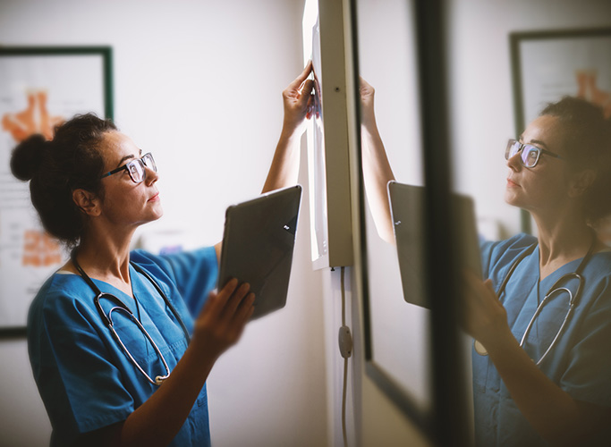 Side view of smiling middle aged nurse checking X-ray in a docto