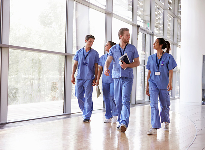 Four healthcare workers in scrubs walking in corridor